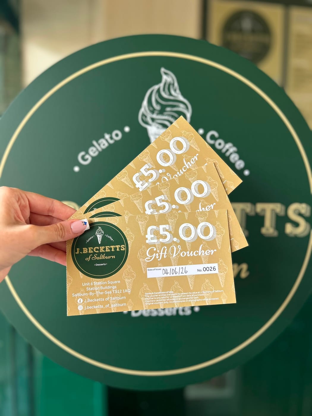 Three J.Becketts of Saltburn £5 gift vouchers held up in front of the shop's green roundel sign