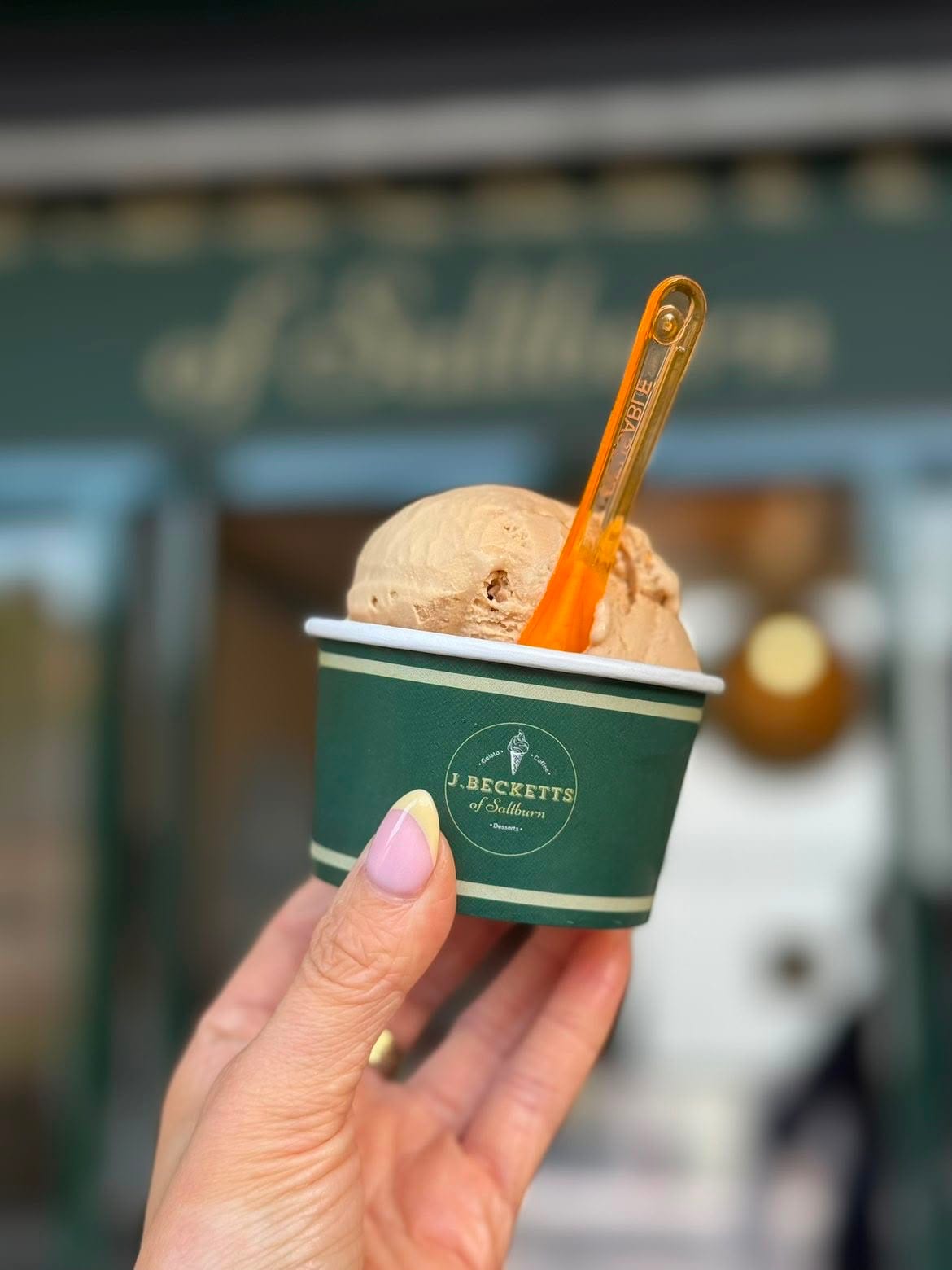 A tub of scoop ice cream held up in front of the J.Becketts of Saltburn shopfront