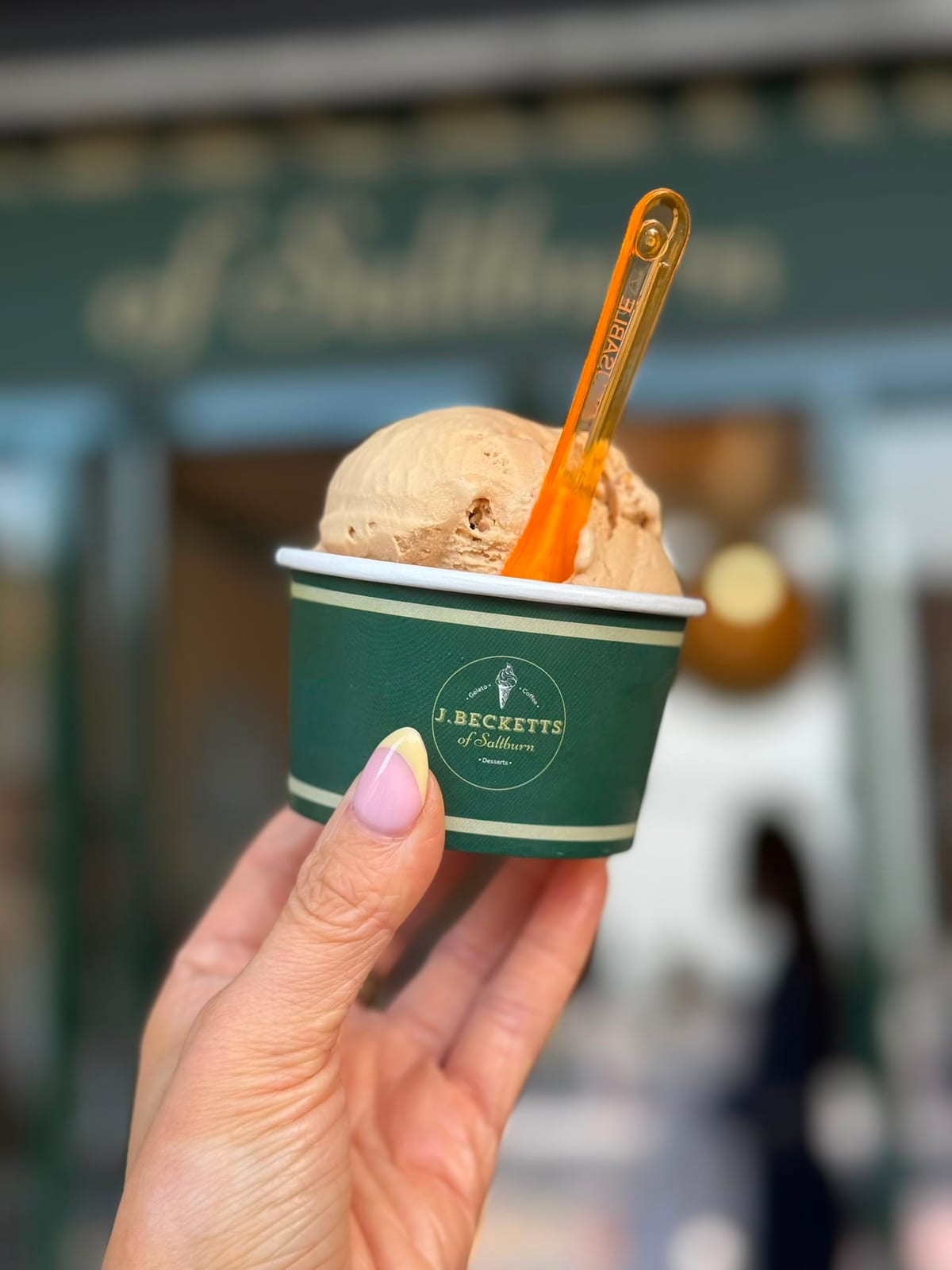 A tub of scoop ice cream held up in front of the J.Becketts of Saltburn shopfront