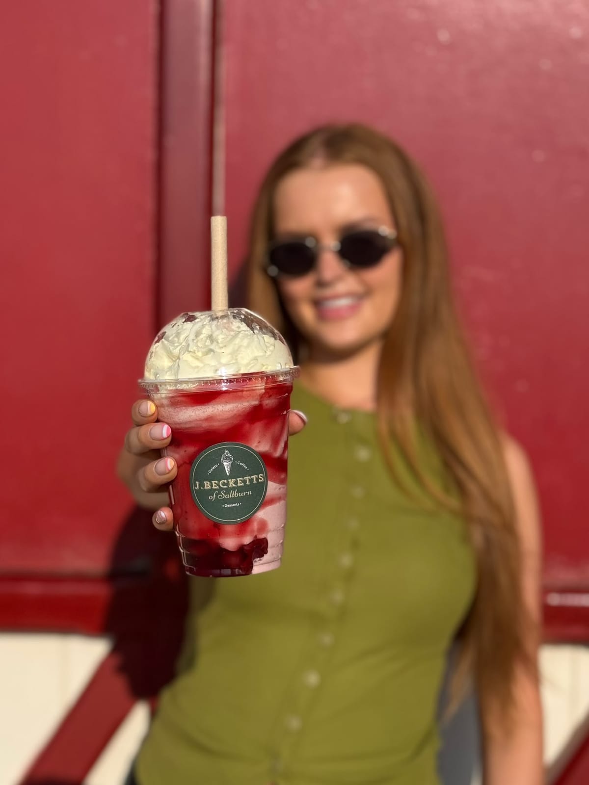 A berry milkshake topped with whipped cream, held up outside J.Becketts of Saltburn